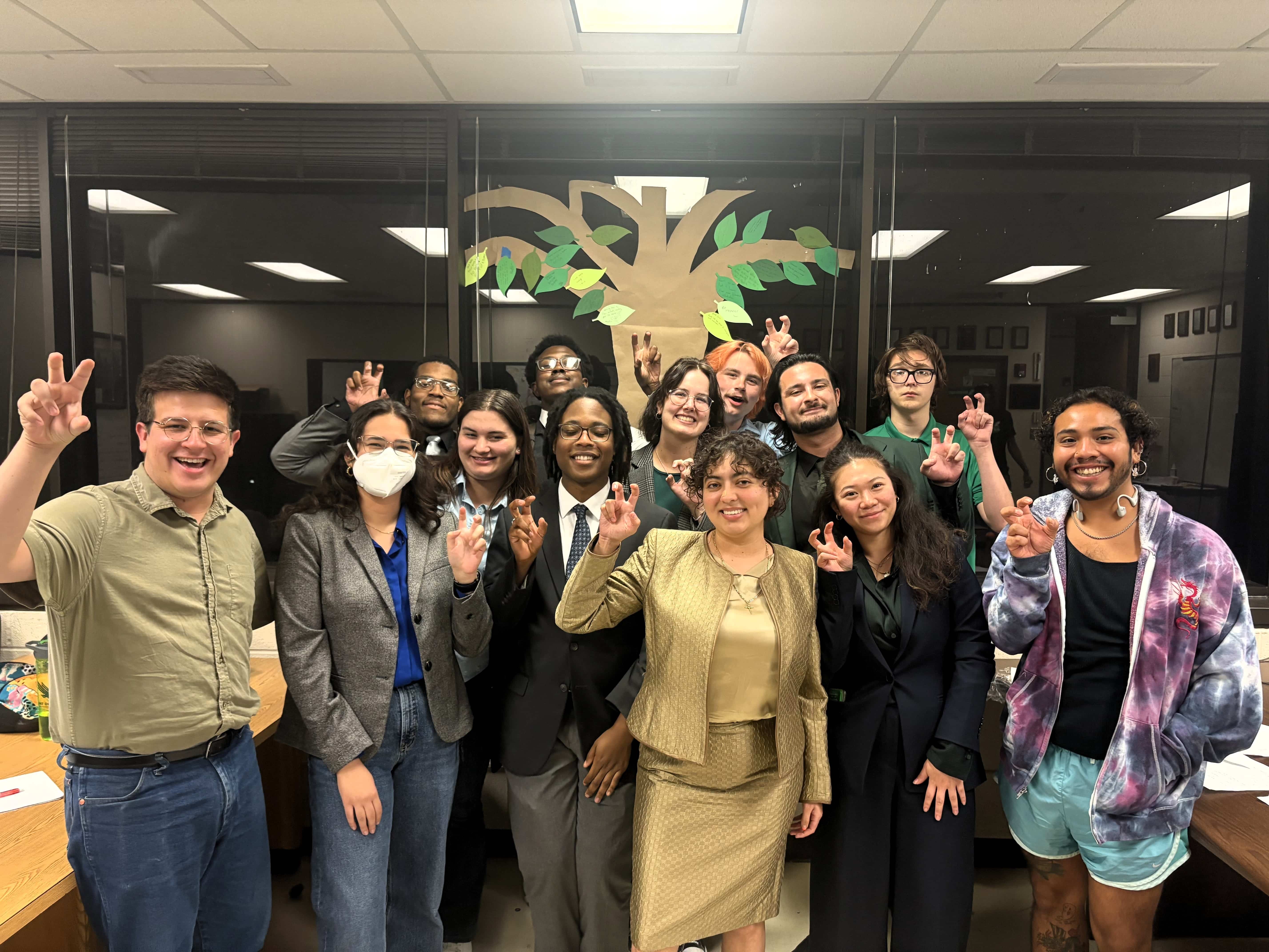 UNT Debate team members smiling for picture and holding their right hands up in UNT claw